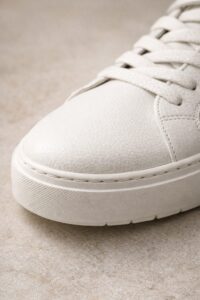 Close-up detail of a crisp white waterproof leather sneaker, showcasing the smooth round toe, clean stitching, and durable textured rubber outsole.