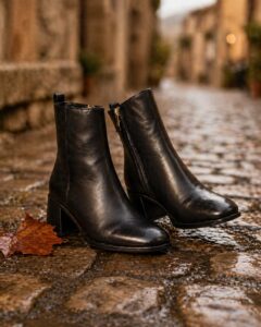 Black leather ankle boots with block heel on wet cobblestones with autumn leaf in Italy