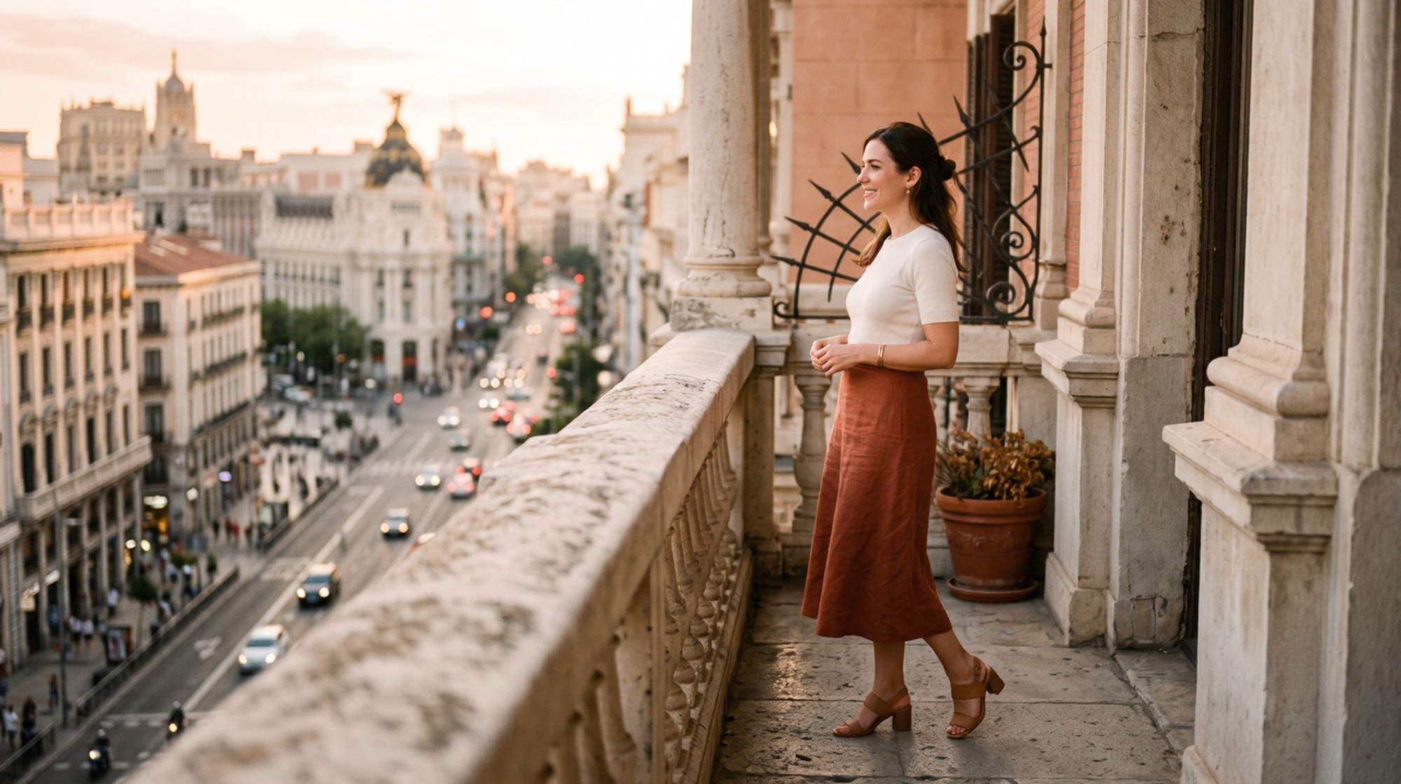 Woman in terracotta linen skirt and ivory top on a Madrid balcony overlooking the Gran V&iacute;a at golden hour