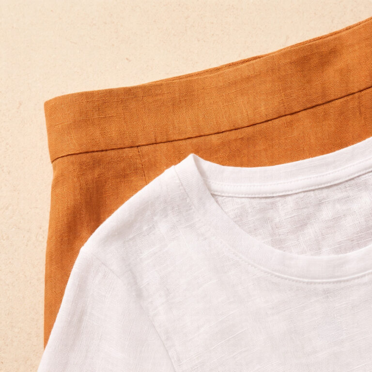 Close-up of Dali ochre linen midi skirt waistband meeting bleached white linen top tucked inside, warm and cool linen weave contrast in afternoon light