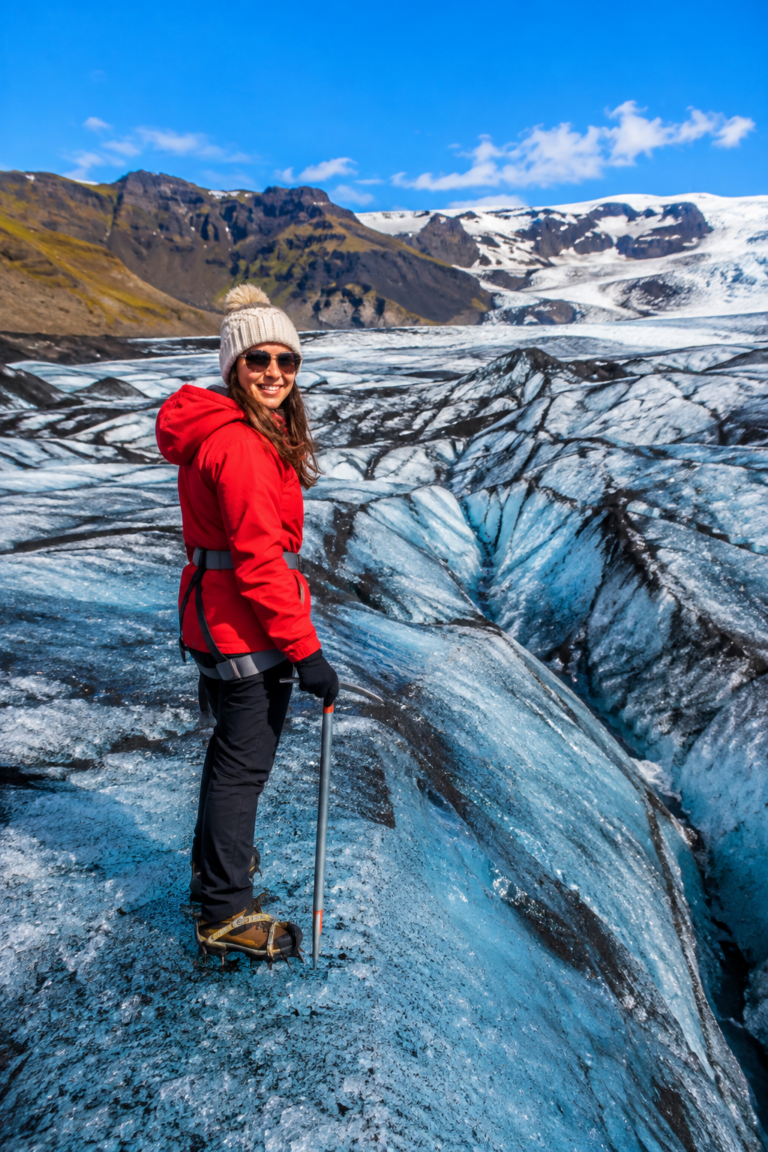 Woman in a red jacket walking on turquoise glacier ice at Solheimajokull with crampons