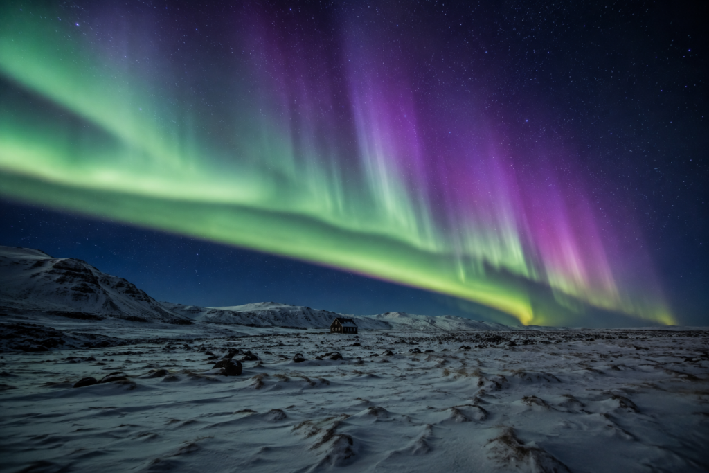Green and violet Northern Lights over a snow-covered Icelandic landscape