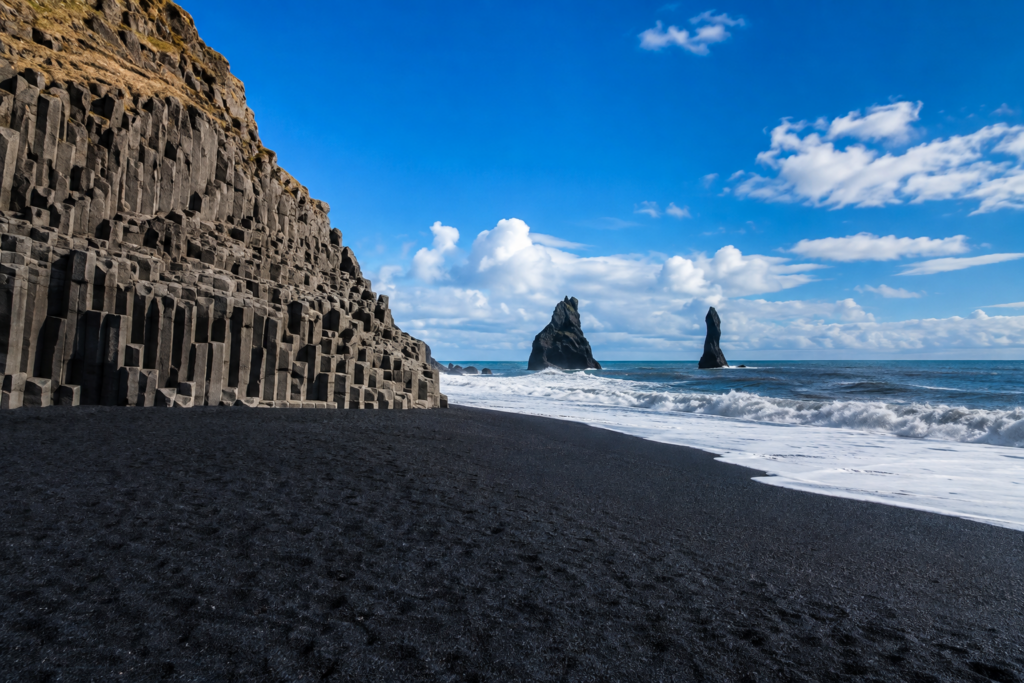 Black sand beach in Iceland with volcanic rock columns and sea stacks rising from the ocean